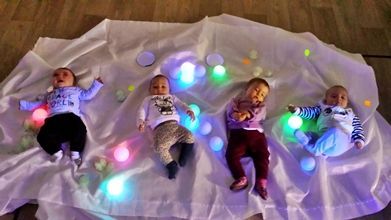 Cuatro bebés están acostados sobre una manta con luces sobre ellos.
