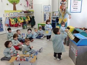 Un grupo de niños está sentado en el suelo frente a un contenedor de reciclaje.