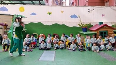 Una mujer con un disfraz de dinosaurio está parada frente a un grupo de niños.