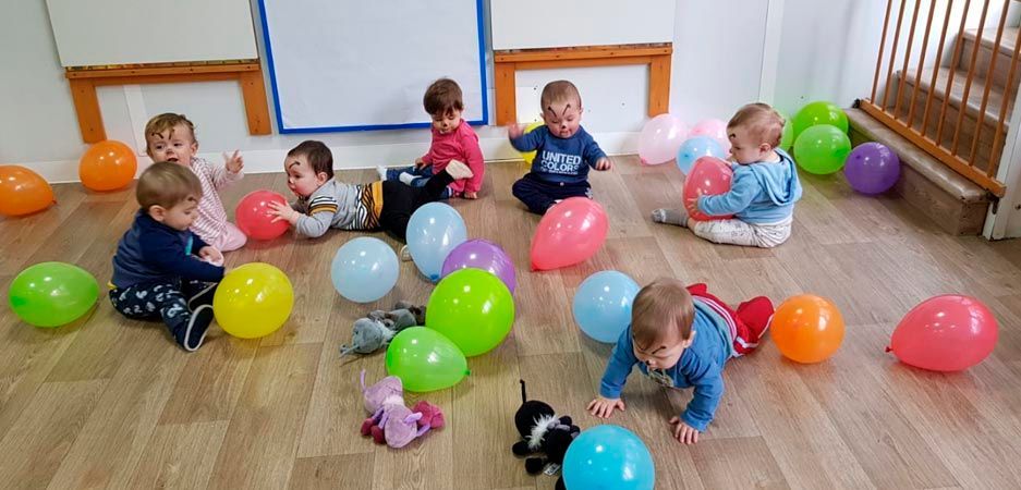 Un grupo de bebés están sentados en el suelo rodeados de globos.