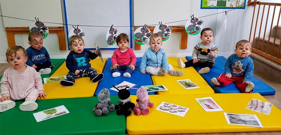 Un grupo de bebés está sentado sobre colchonetas en un aula.