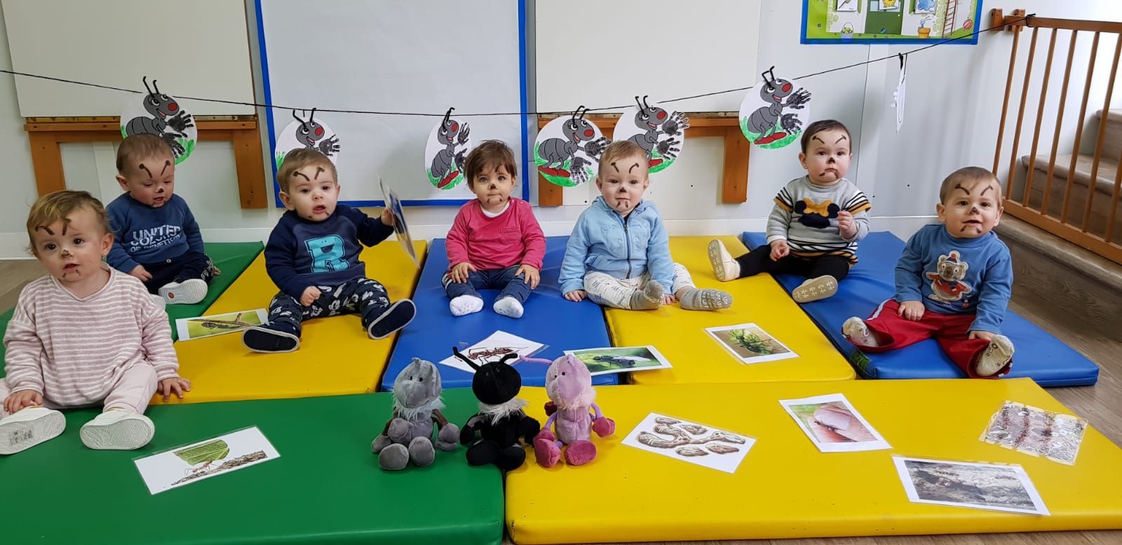 Un grupo de bebés está sentado sobre colchonetas en una habitación.