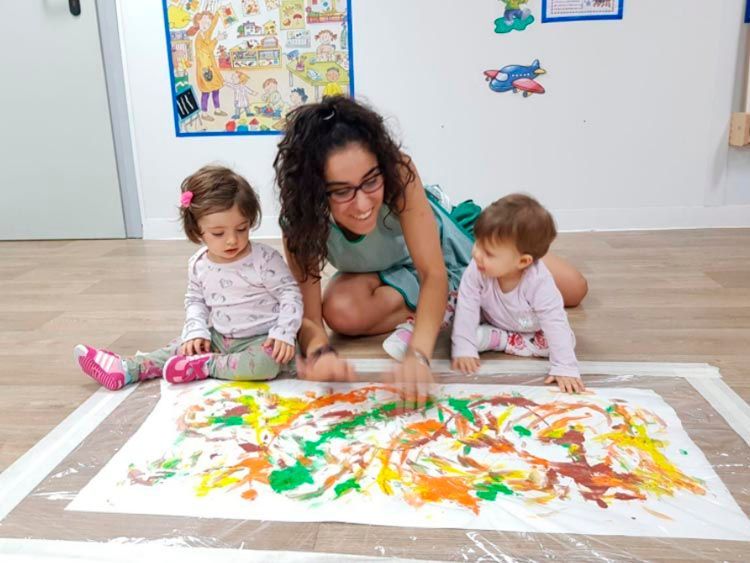 Una mujer y dos bebés están jugando con pintura en un trozo grande de papel.