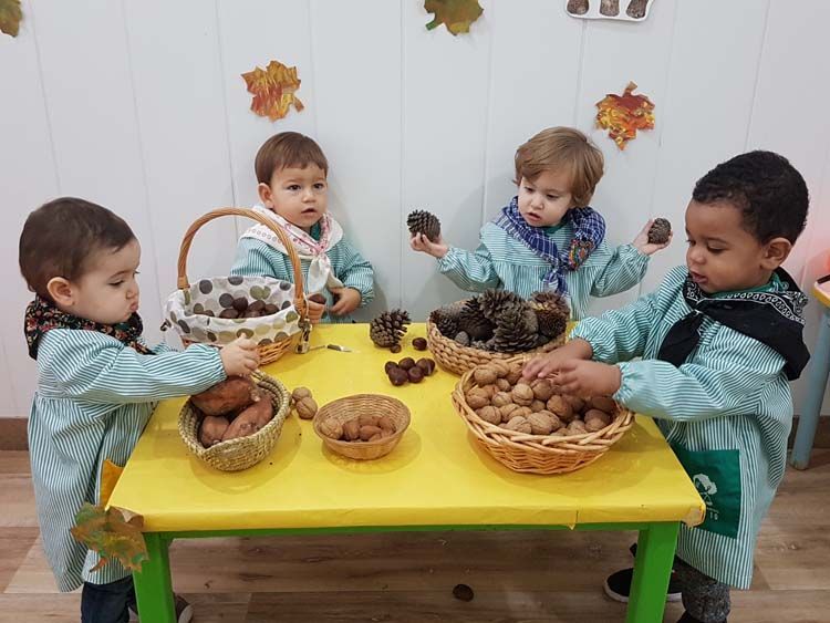 Un grupo de niños pequeños está sentado en una mesa jugando con piñas.