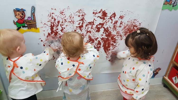Tres bebés están pintando en una pared con pintura roja.