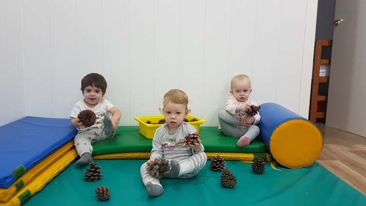 Un grupo de bebés está sentado en una estera sosteniendo piñas.