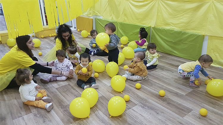 Un grupo de niños está sentado en el suelo jugando con globos amarillos.