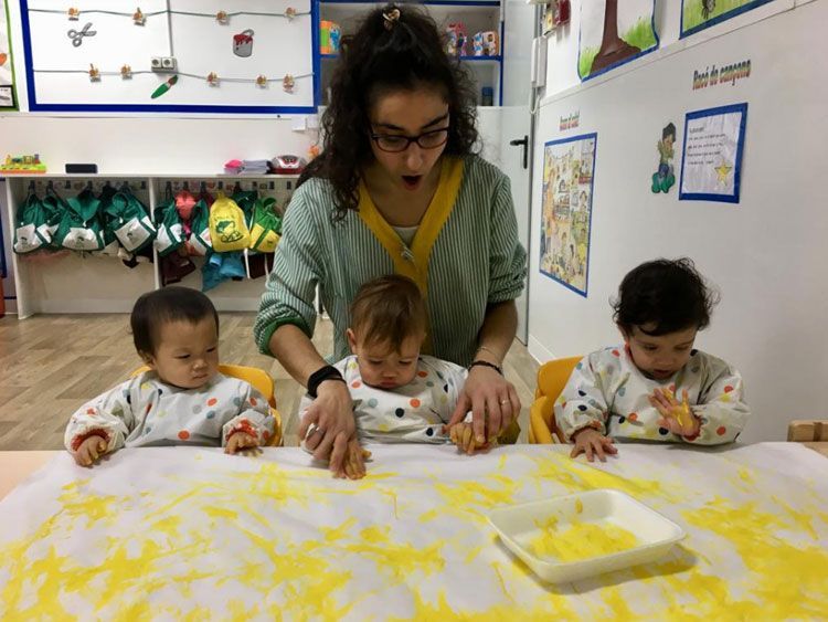 Un grupo de bebés está jugando con polvo amarillo sobre una mesa.