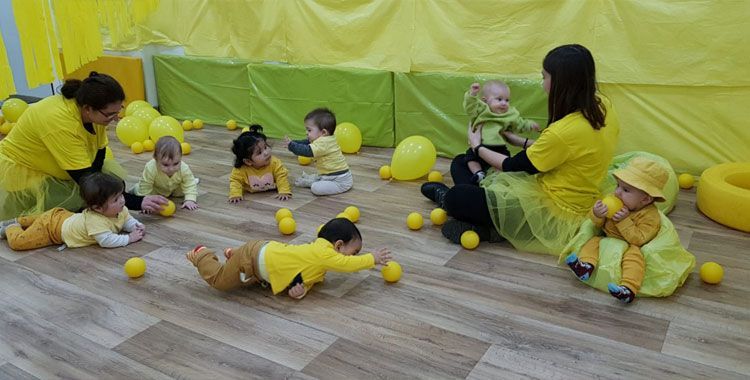 Un grupo de bebés está jugando con pelotas amarillas en una habitación.