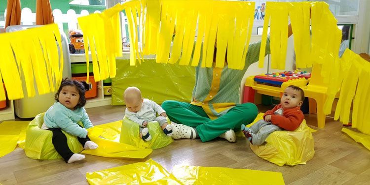 Tres bebés están sentados en pufs amarillos en una habitación.