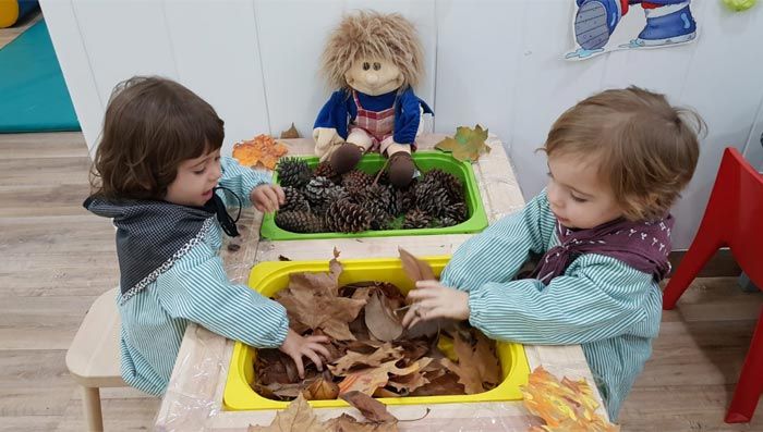 Dos niñas juegan con hojas y piñas en una mesa.