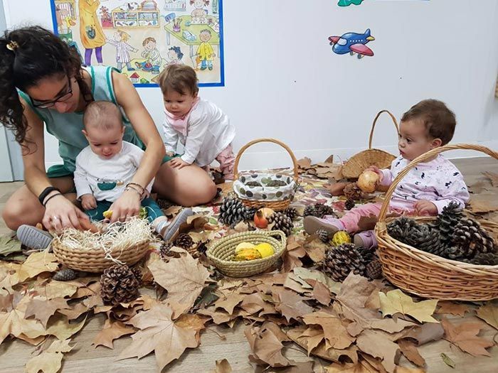 Una mujer está sentada en el suelo con tres bebés jugando con hojas y piñas.