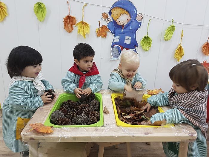 Un grupo de niños está jugando con piñas y hojas en una mesa.