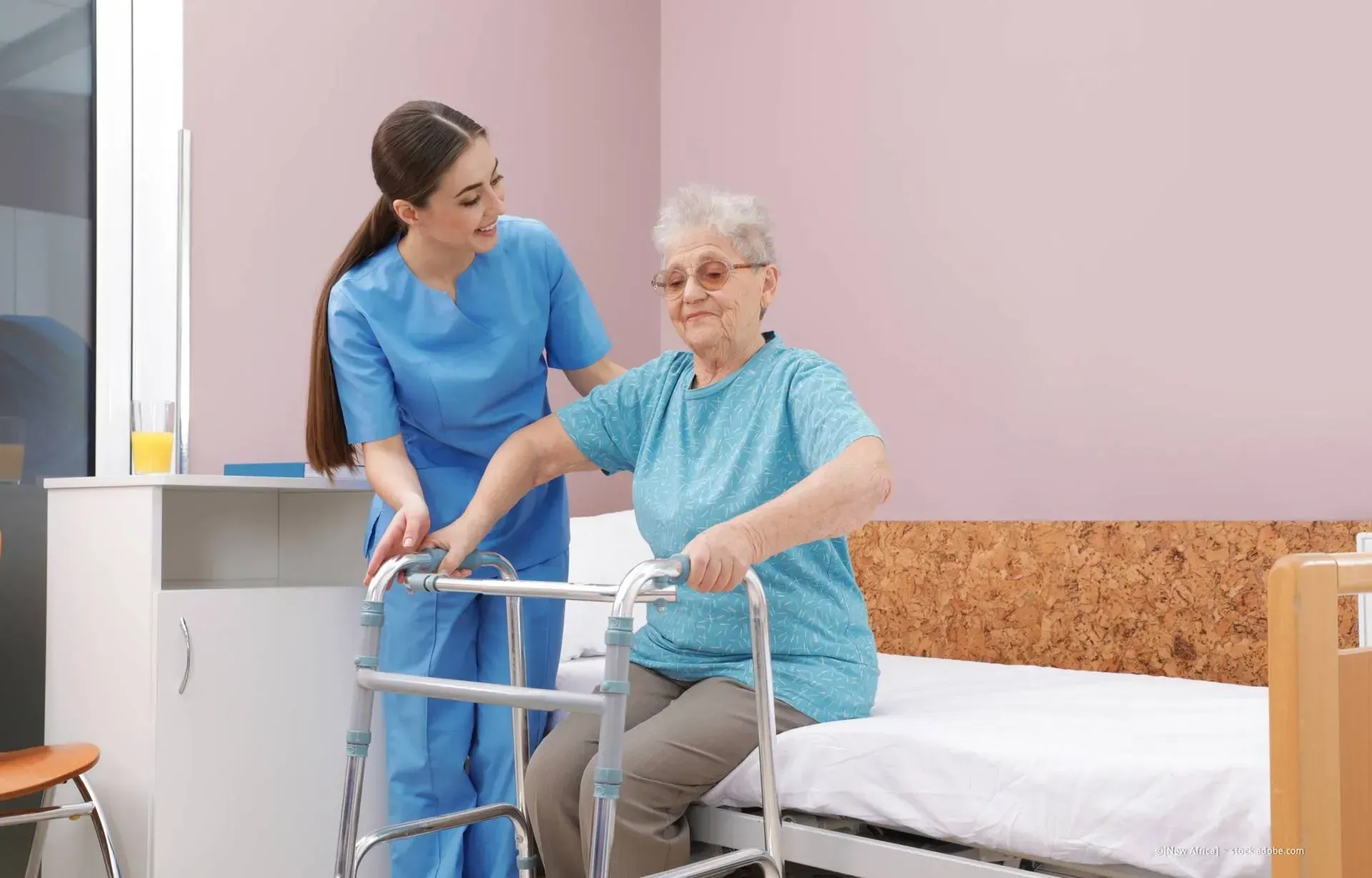 Krankenschwester hilft einem Patienten mit einem Rollator in einem Krankenzimmer