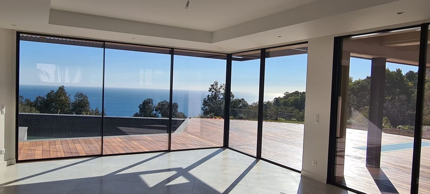 Salon moderne avec baies vitrées offrant une vue imprenable sur l'océan et une terrasse ensoleillée