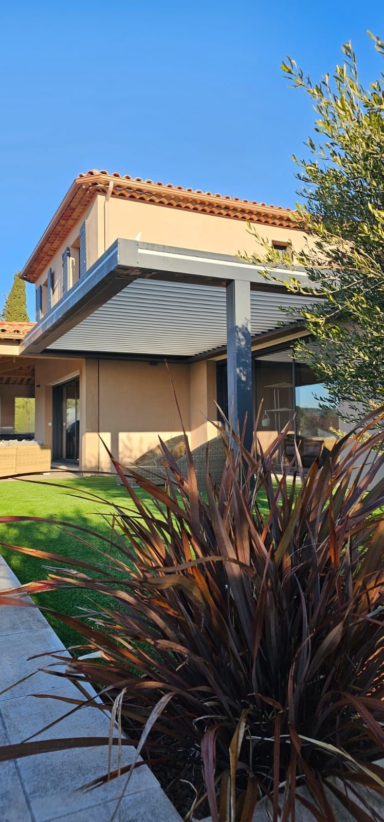 Extérieur d'une maison moderne à deux étages avec murs blancs, porte de garage foncée et claustra vertical en bois à l'étage supérieur