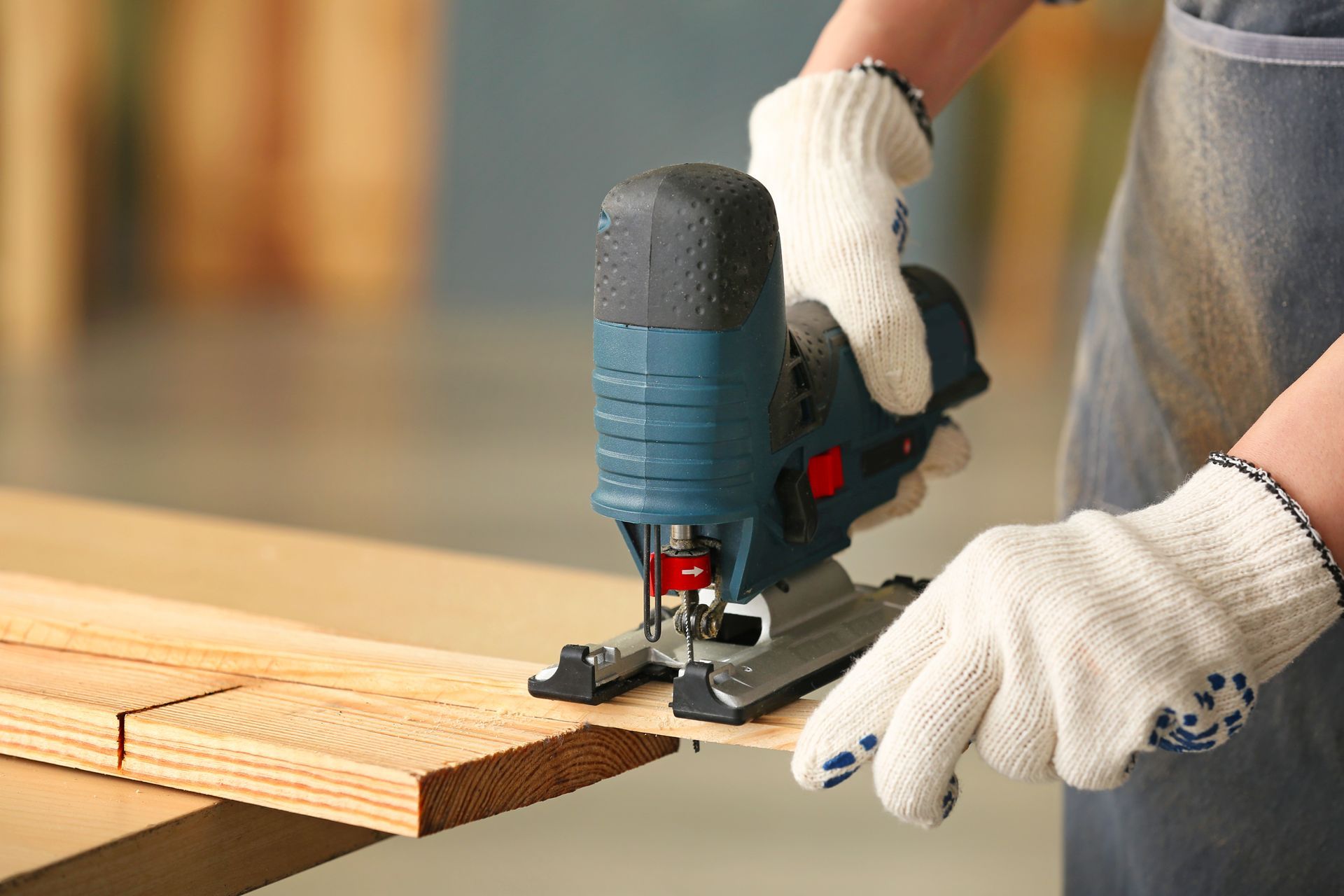 Des mains gantées de blanc utilisent une scie sauteuse pour découper des planches en bois sur un établi.