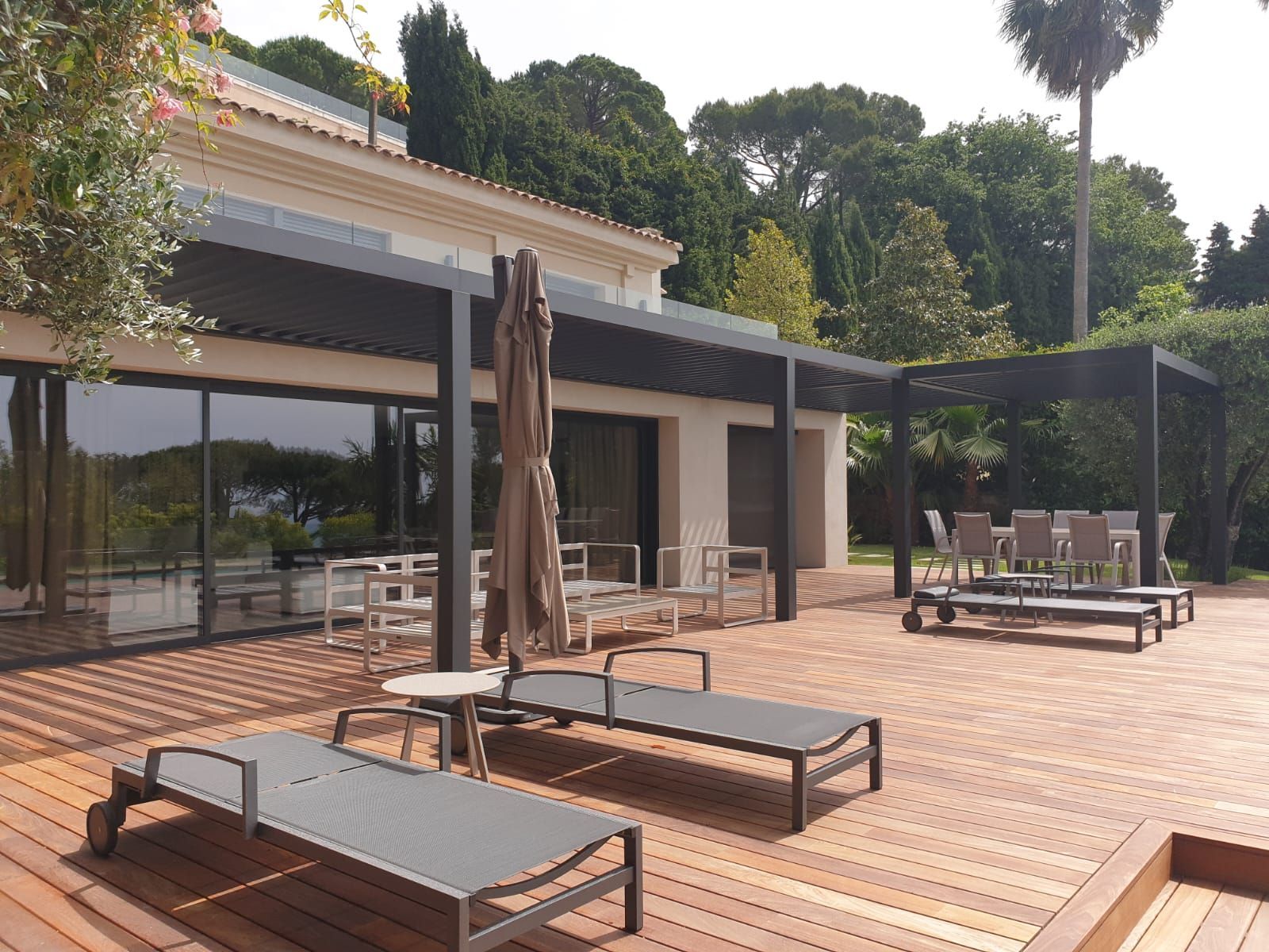 Terrasse extérieure avec chaises longues, tables, parasols et un bâtiment moderne sous les arbres.
