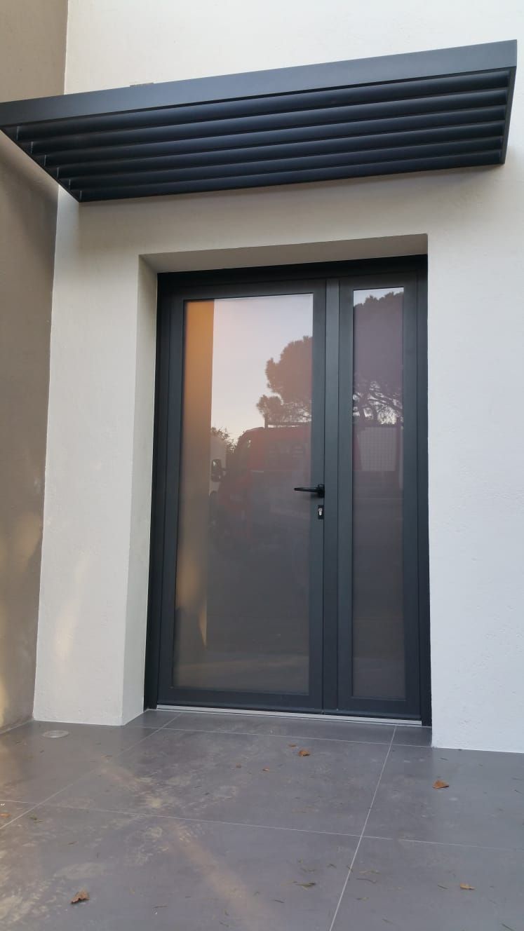 Entrée principale avec une porte en verre foncé et un auvent noir au-dessus d'un mur extérieur blanc.