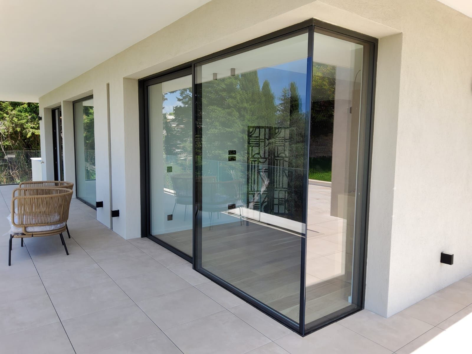 Patio moderne avec portes vitrées du sol au plafond, murs blancs et fauteuil en osier sur sol carrelé