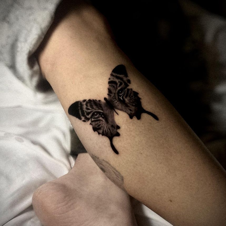 Un tatuaje de una mariposa en blanco y negro en un brazo, con rayas de tigre y ojos estampados en las alas.