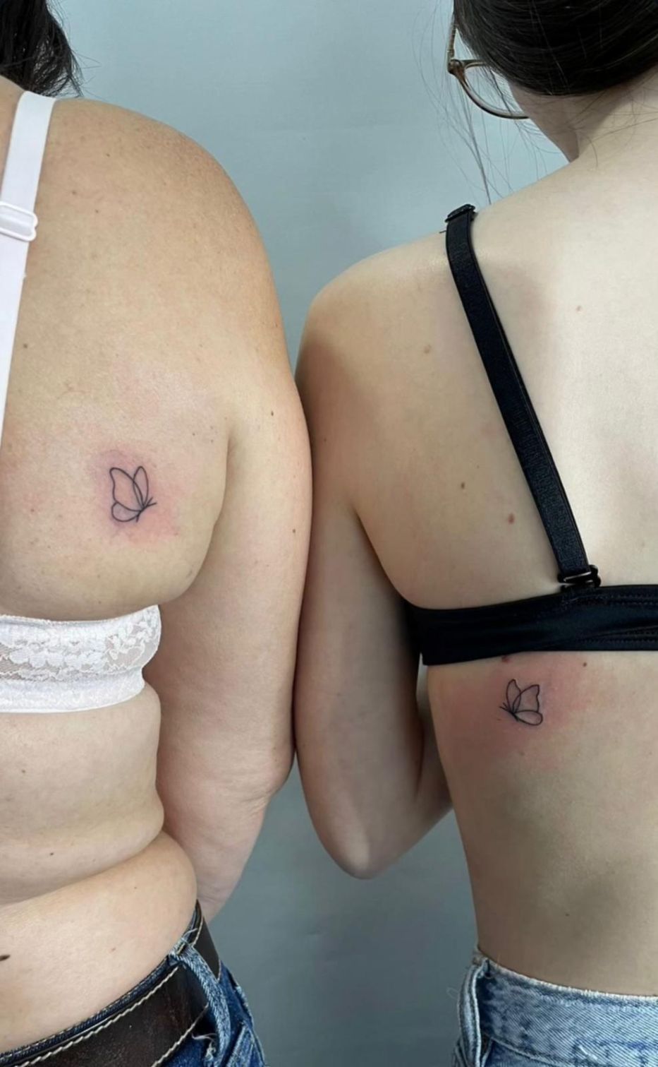 Dos personas , cada una mostrando un pequeño y delicado tatuaje con el contorno de una mariposa en su espalda.