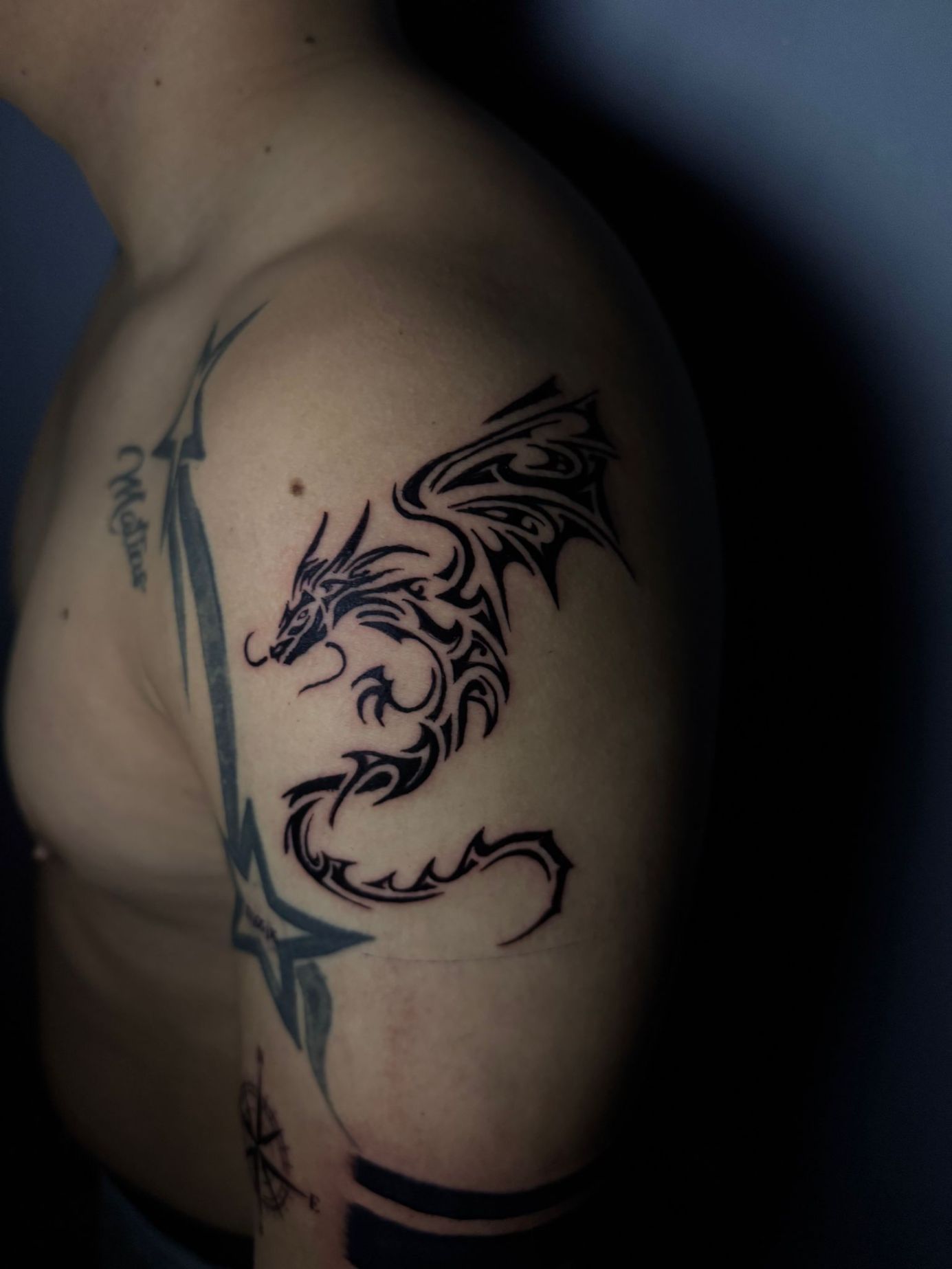 Un tatuaje de un dragón negro de estilo tribal en la parte superior del brazo de una persona