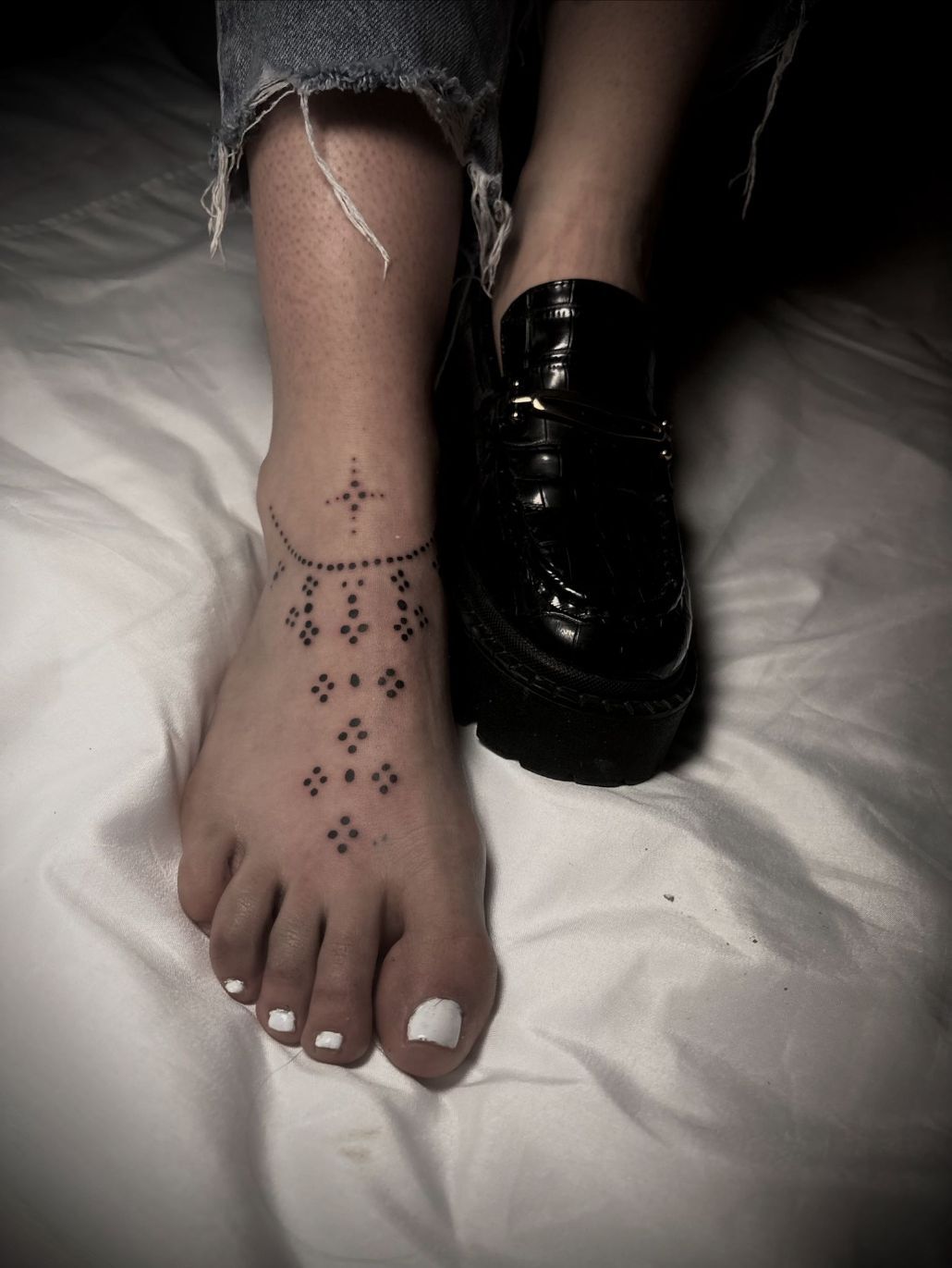Un pie con un delicado tatuaje geométrico de estrella y punto en la parte superior