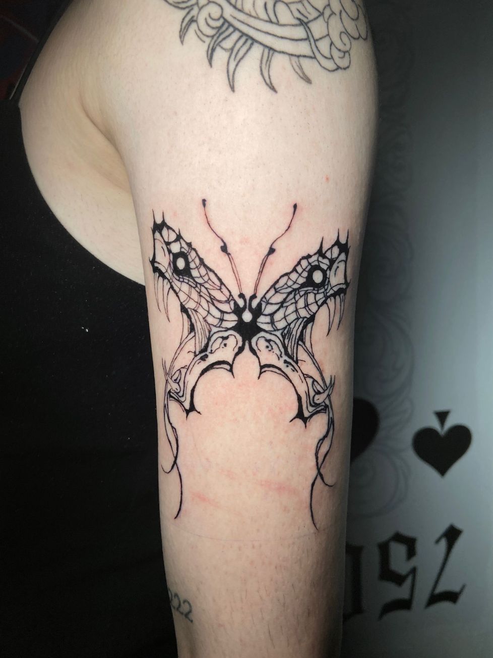 Un tatuaje de mariposa de estilo gótico, hecho con tinta negra, en la parte superior del brazo