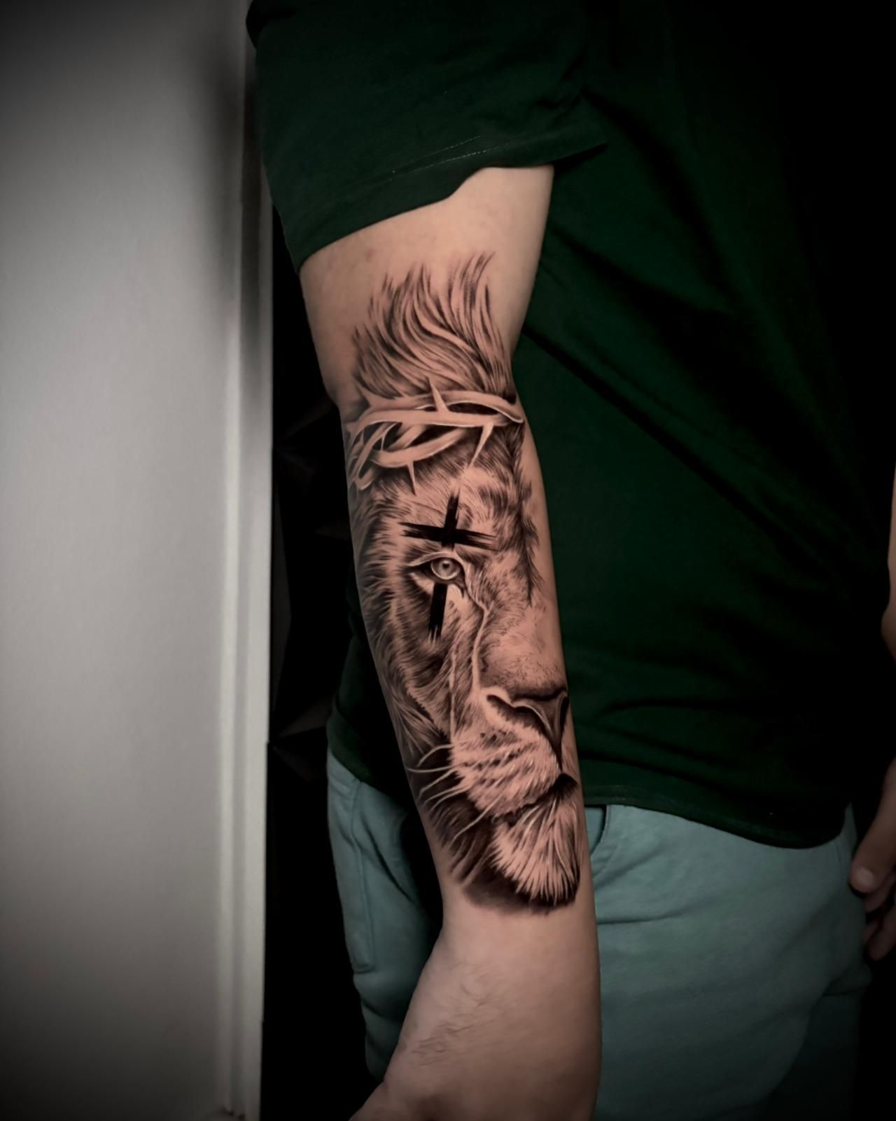 Tatuaje en blanco y negro de un león con una corona de espinas y una cruz sobre un ojo