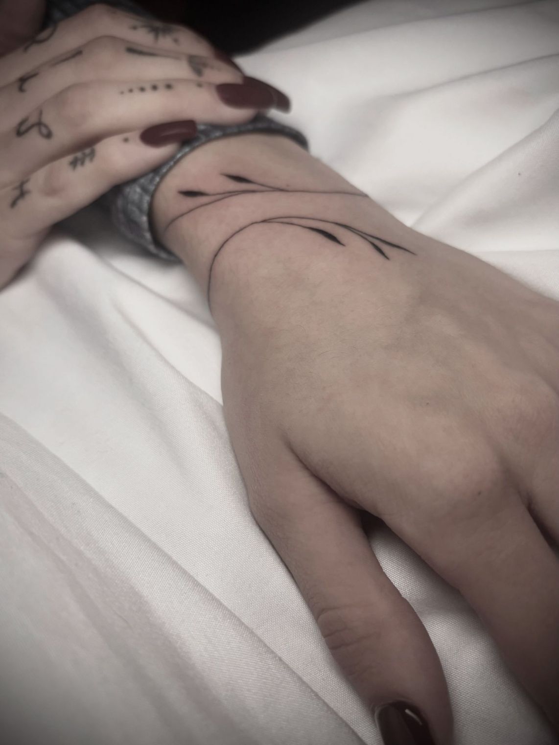 Una mano con pequeños tatuajes en los dedos y luce un delicado tatuaje minimalista en forma de pulsera 