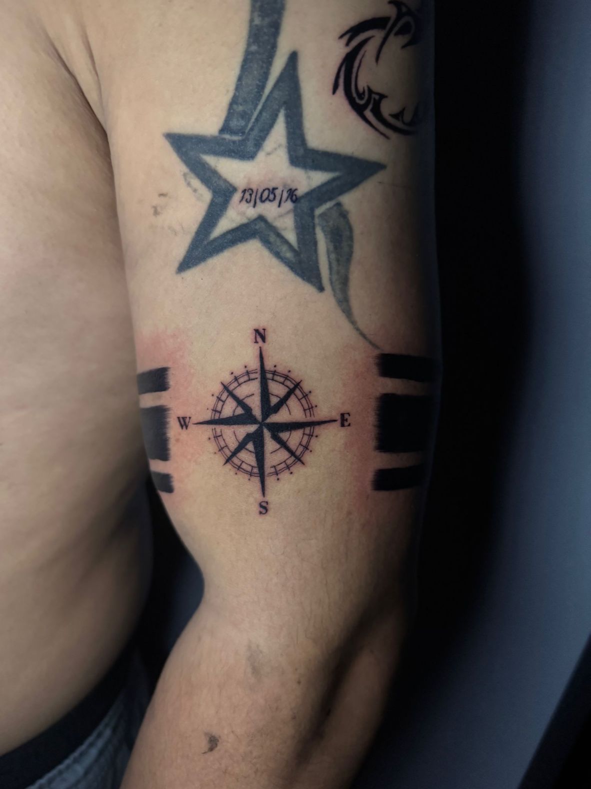 Primer plano de un tatuaje que muestra una rosa de los vientos centrada entre dos gruesas bandas negras en el brazo.