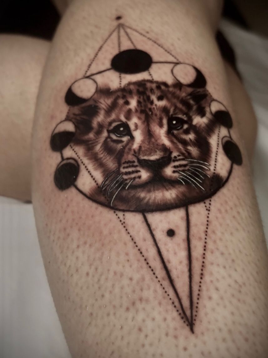 Un tatuaje de la cara de un cachorro de león rodeada por un marco geométrico con las fases lunares 