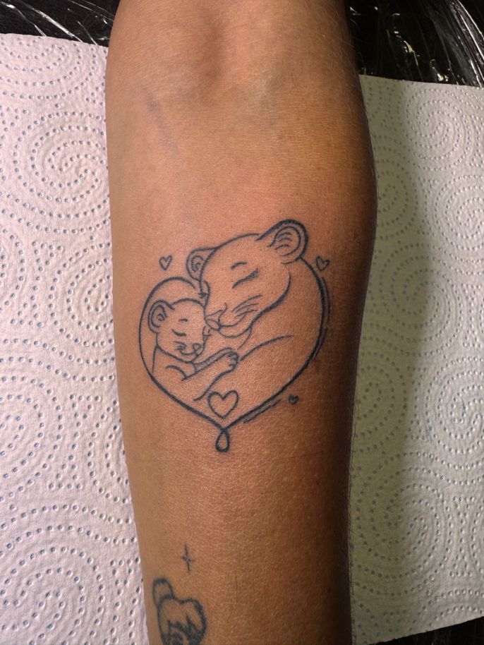 Un tatuaje de líneas finas en el antebrazo que representa a una leona y su cachorro acurrucados