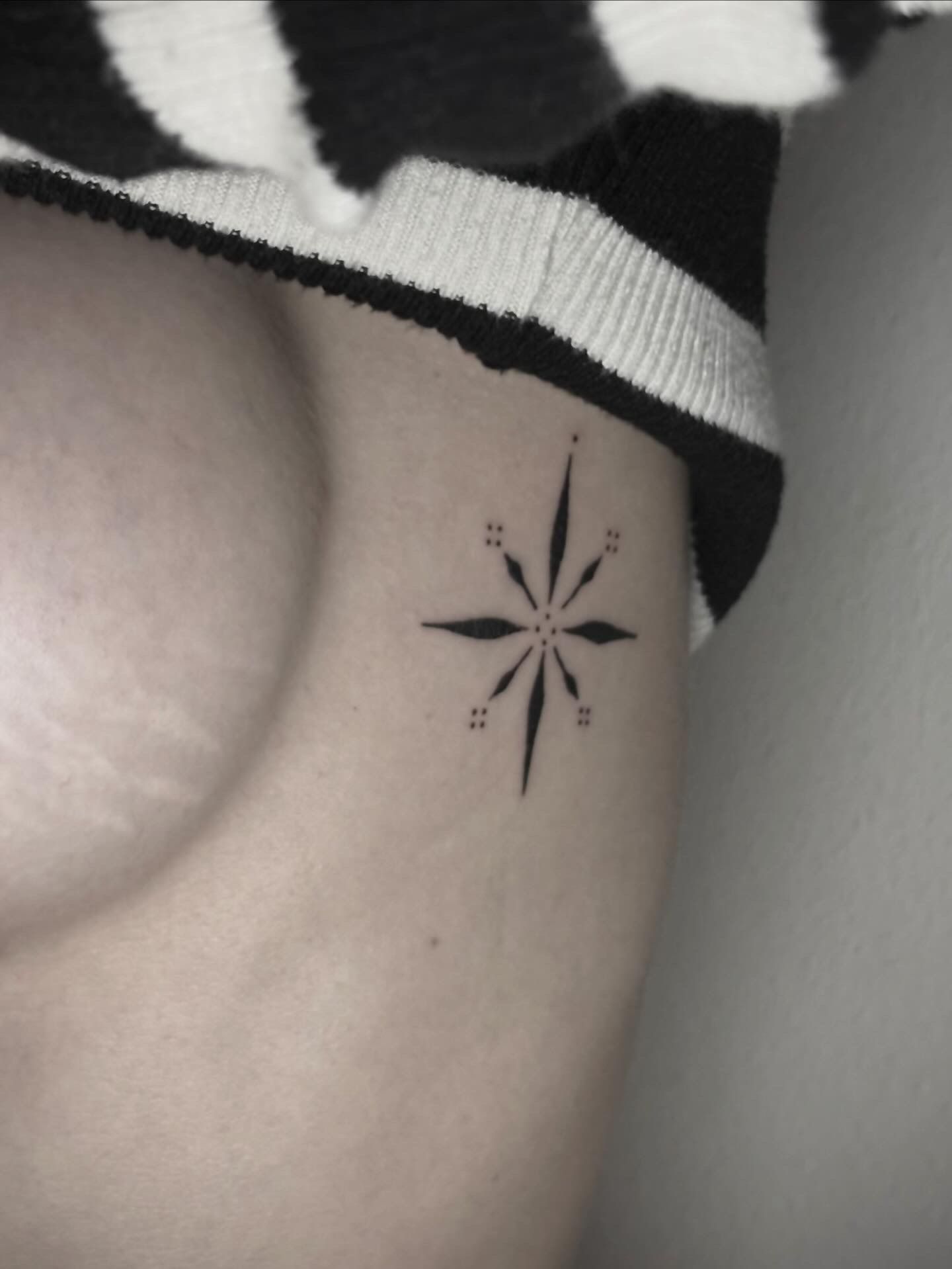 Un tatuaje minimalista en tinta negra que representa una estrella estilizada de ocho puntas, situada en el lateral del torso.