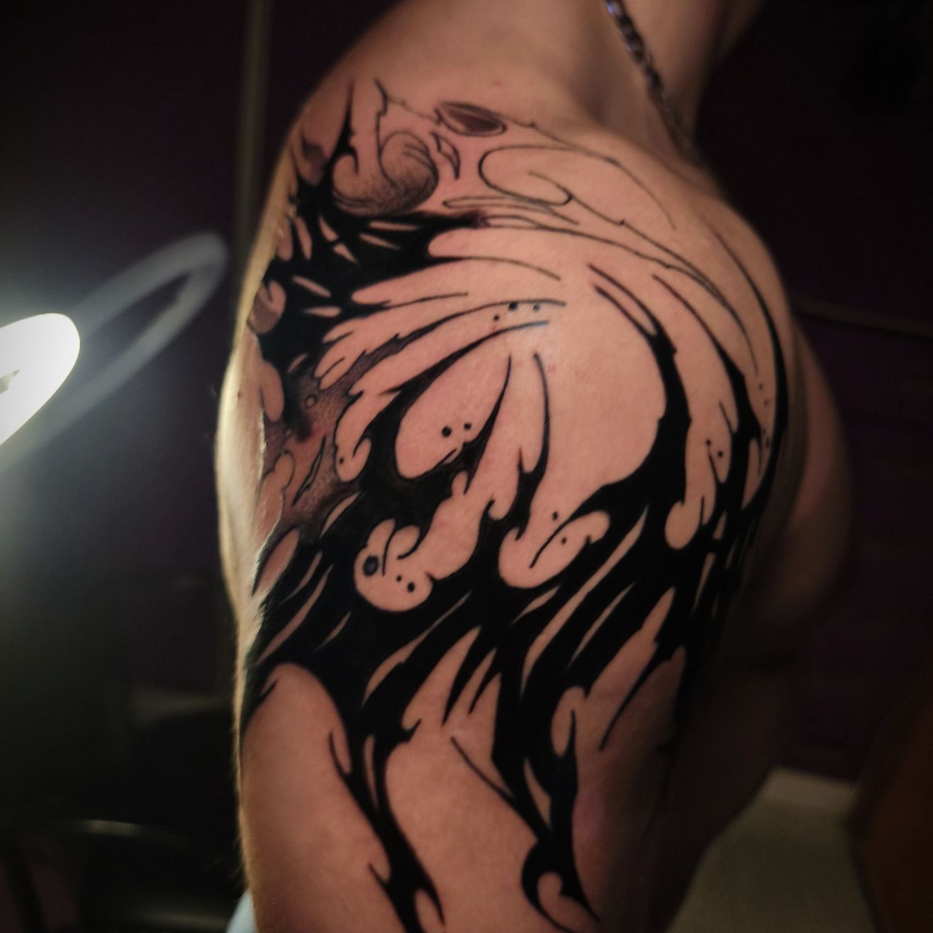 Un tatuaje de estilo tribal en tinta negra en la parte superior del brazo, con formas orgánicas abstractas y fluidas.