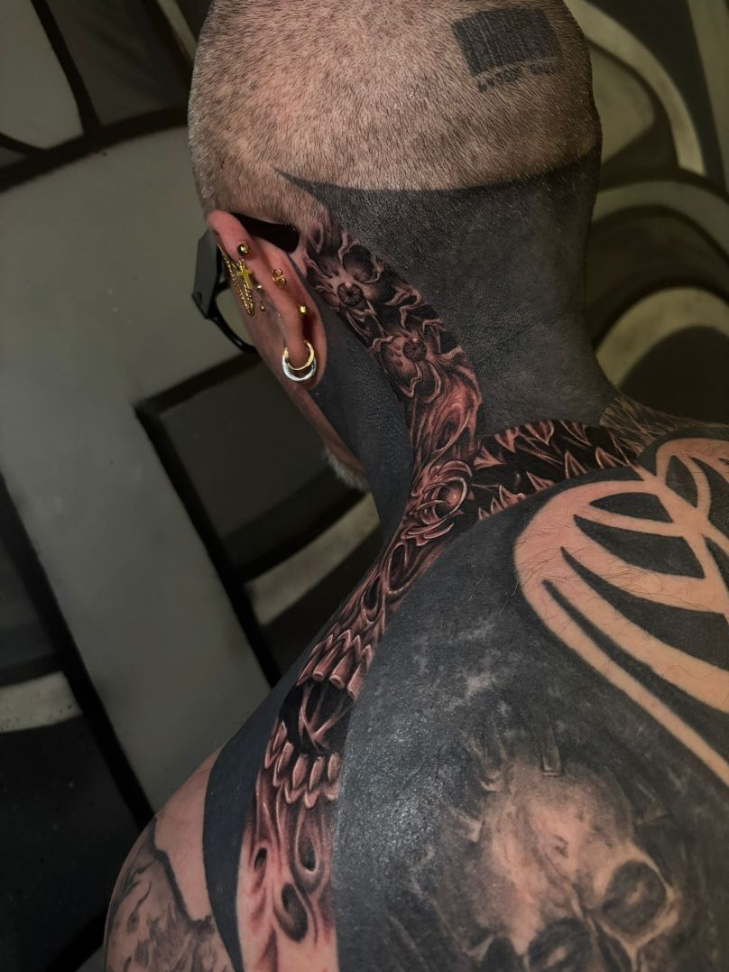 Vista posterior de una persona con la cabeza rapada y extensos tatuajes de estilo blackwork que cubren su cuello