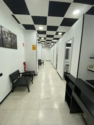 Un pasillo de paredes blancas con techo a cuadros, que cuenta con un banco negro y un mostrador de recepción.