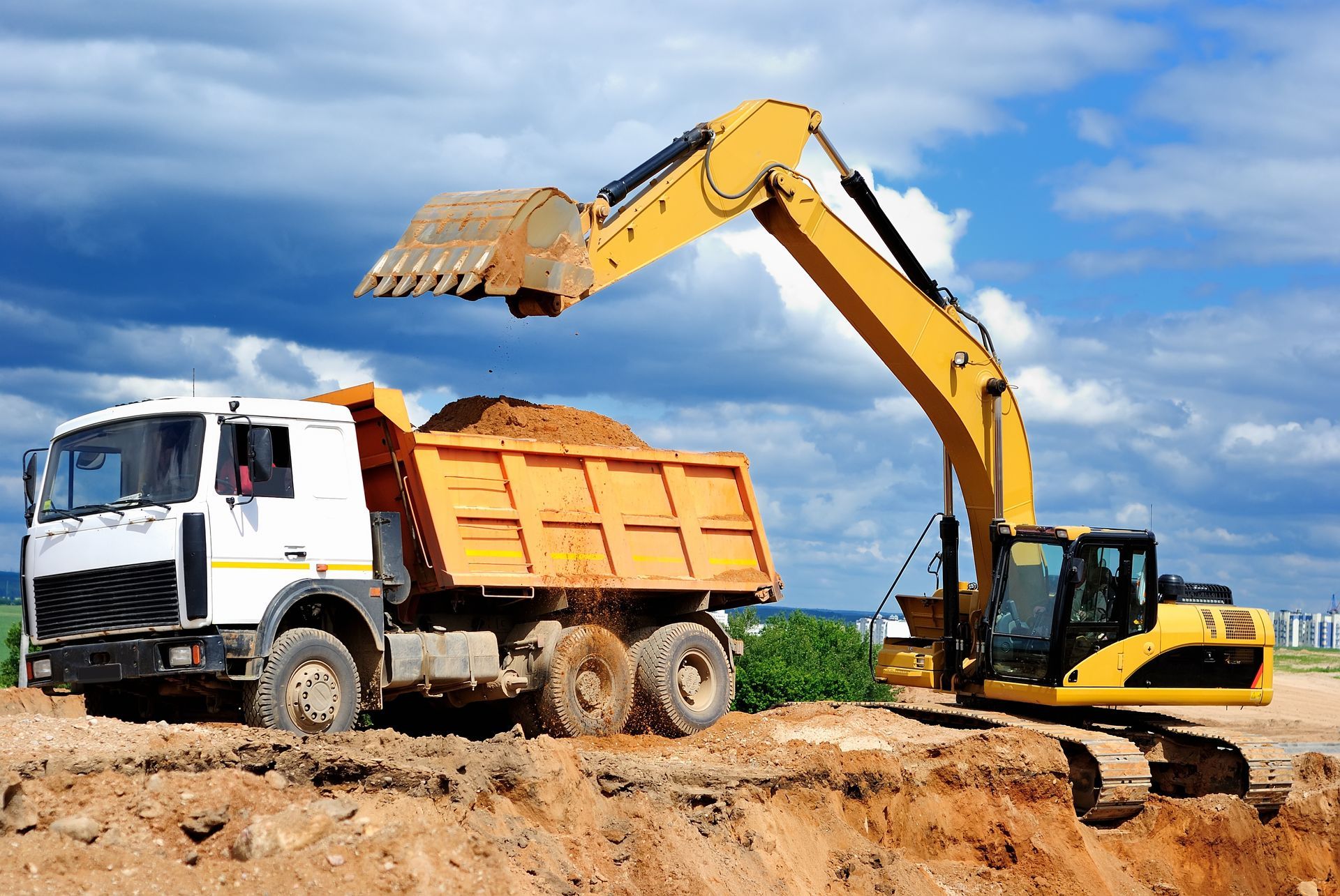 Une pelleteuse jaune charge de la terre dans un camion-benne orange sur un chantier de construction.