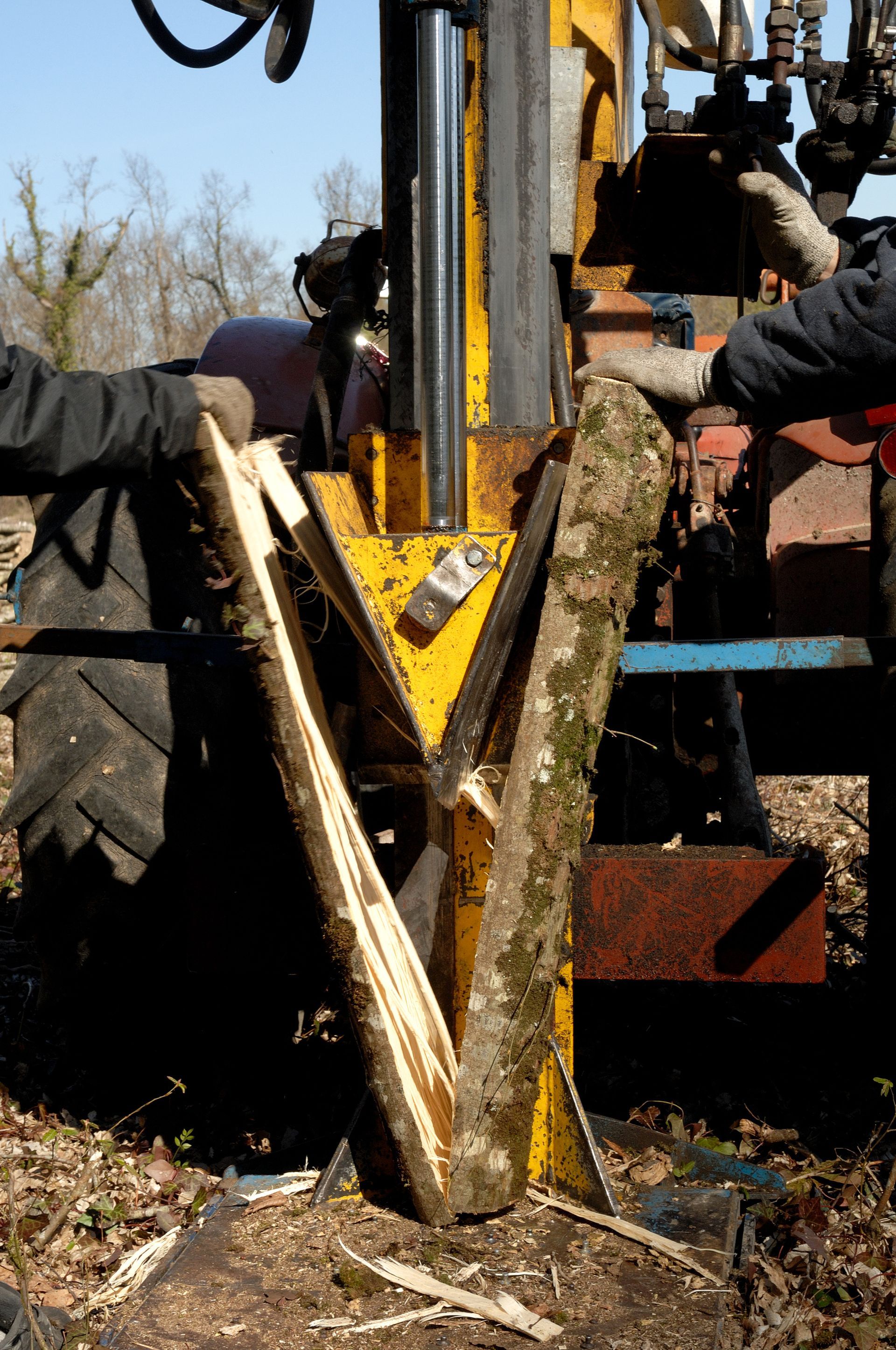 Une bûche est fendue par une fendeuse à bûches jaune, tenue par deux personnes.