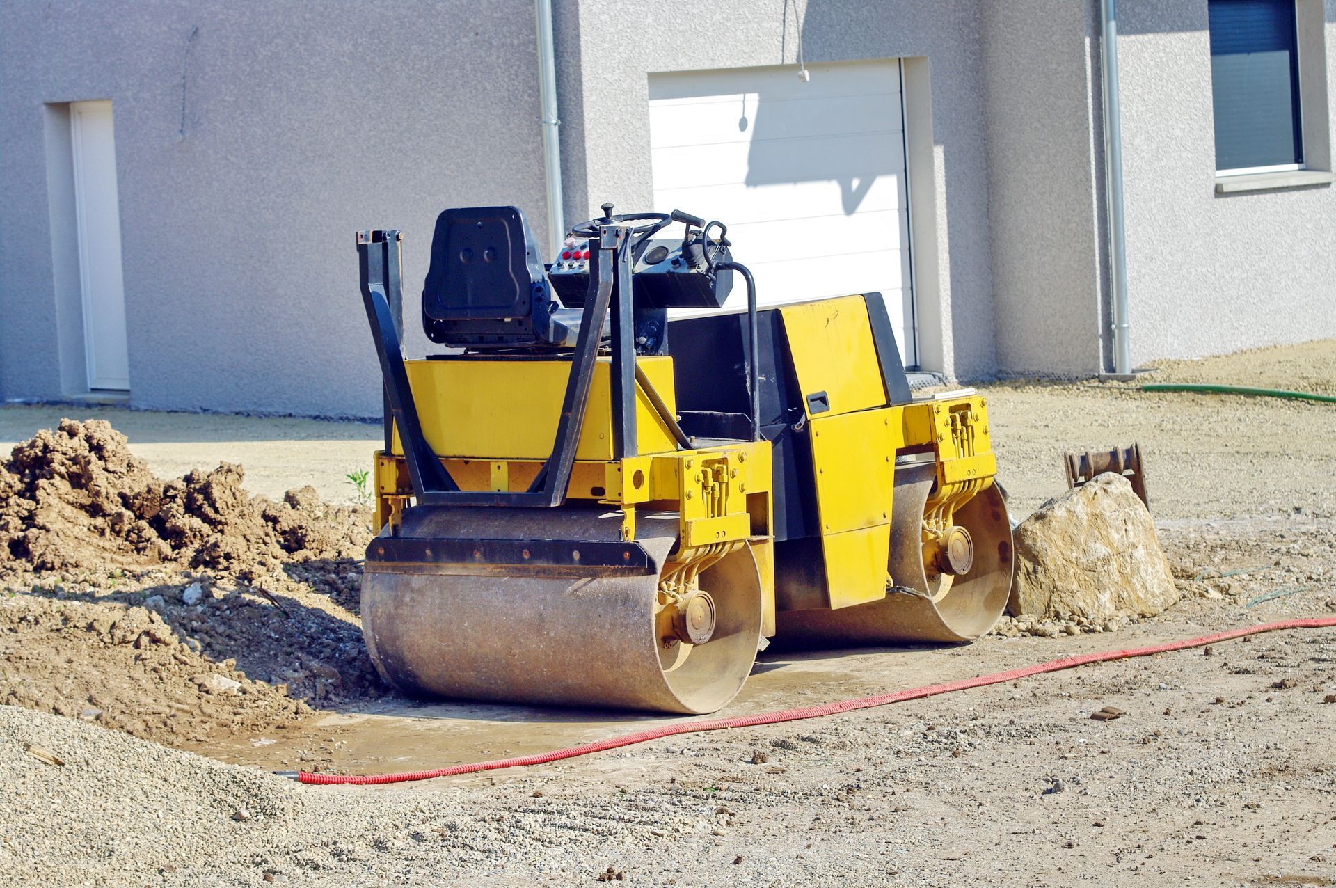 Un rouleau compresseur jaune compacte du gravier près d'une maison.