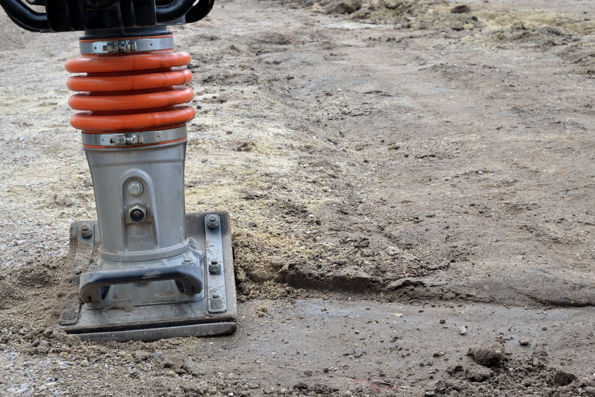 Un piloneuse de sol tasse la terre. La machine est grise et orange.