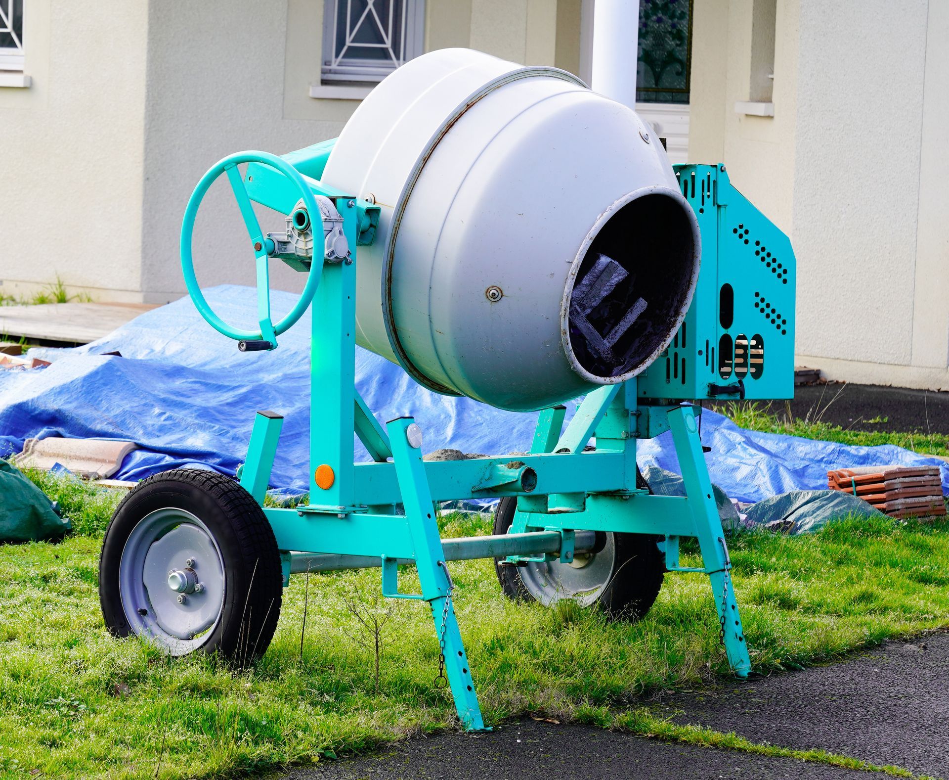 Bétonnière bleue et grise, dans une cour, avec roue, mélangeant des matériaux.