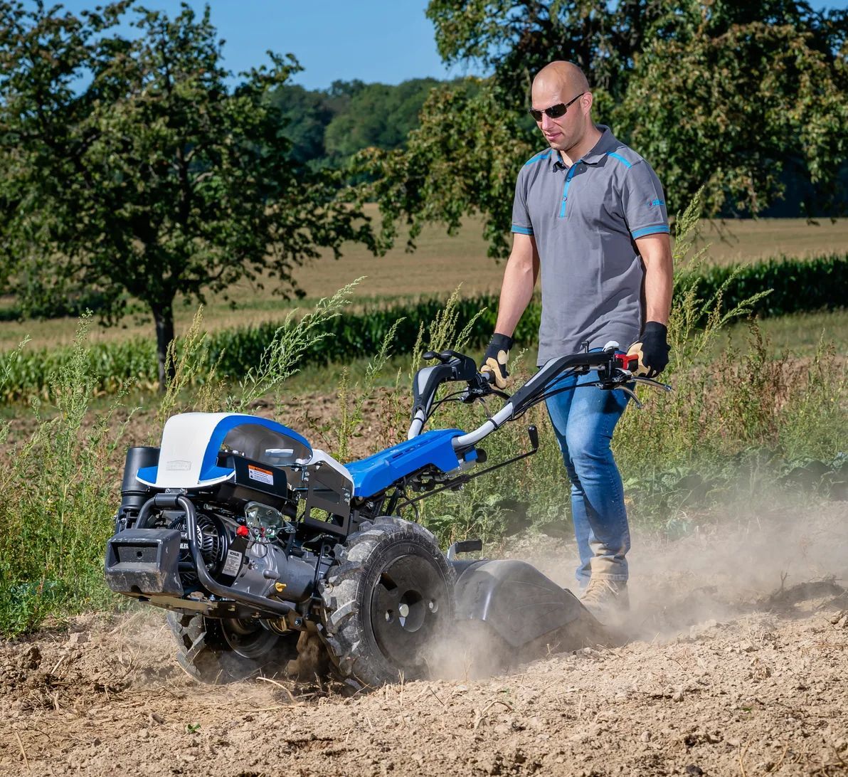 Un homme utilise une motobineuse bleue et blanche dans un champ.