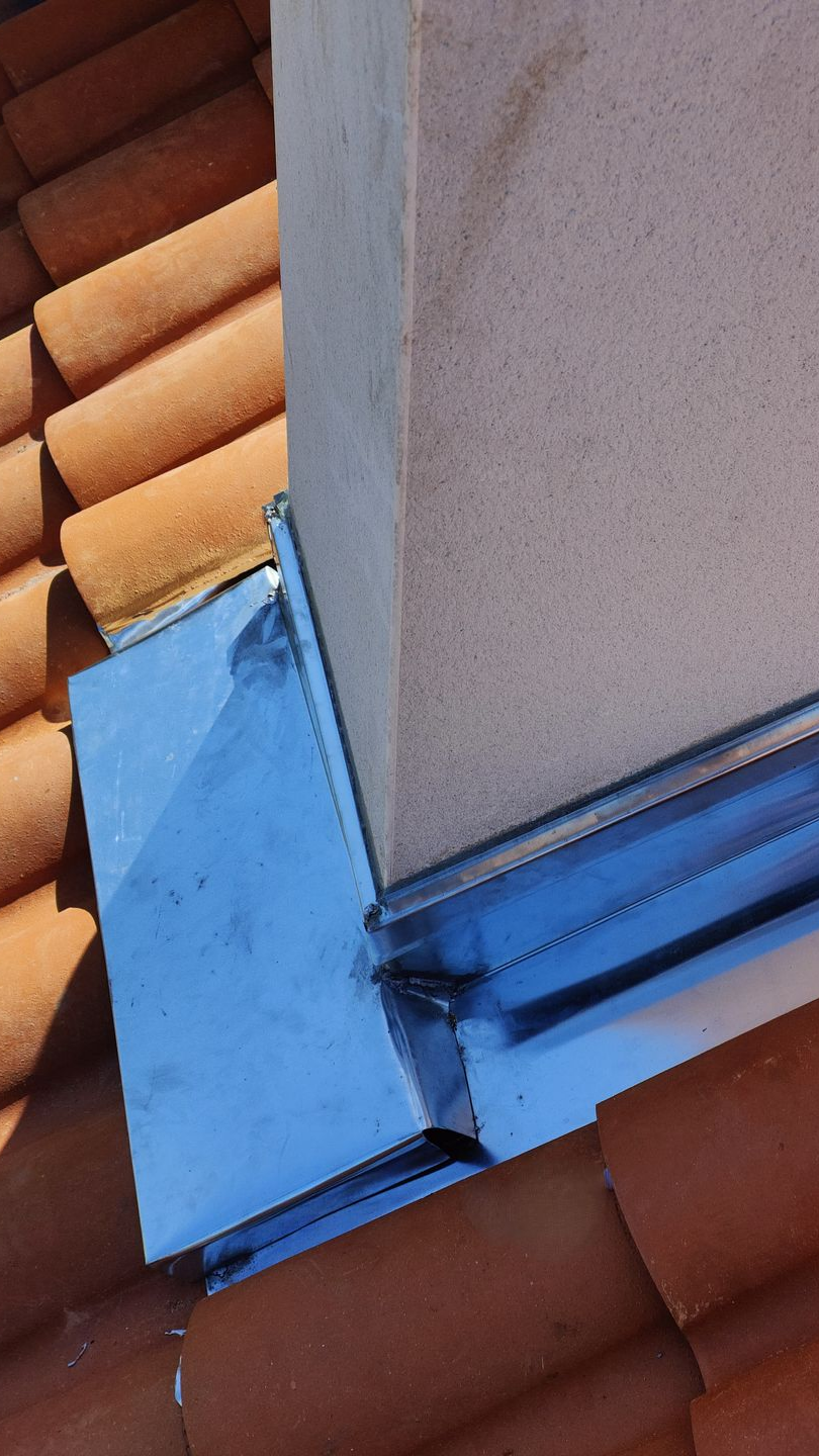 Bande de solin bleue et joint de toiture à l'endroit où un mur beige rencontre des tuiles en terre cuite