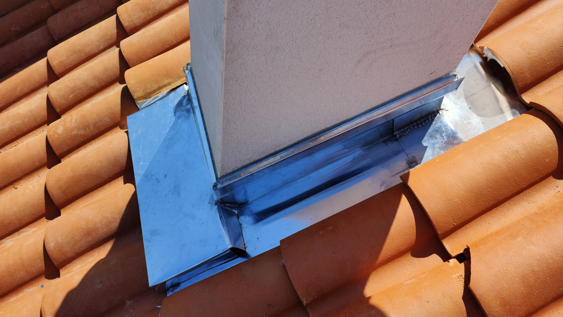 Solin de ventilation de toit sur tuiles en terre cuite orange avec mastic d'étanchéité bleu à la base