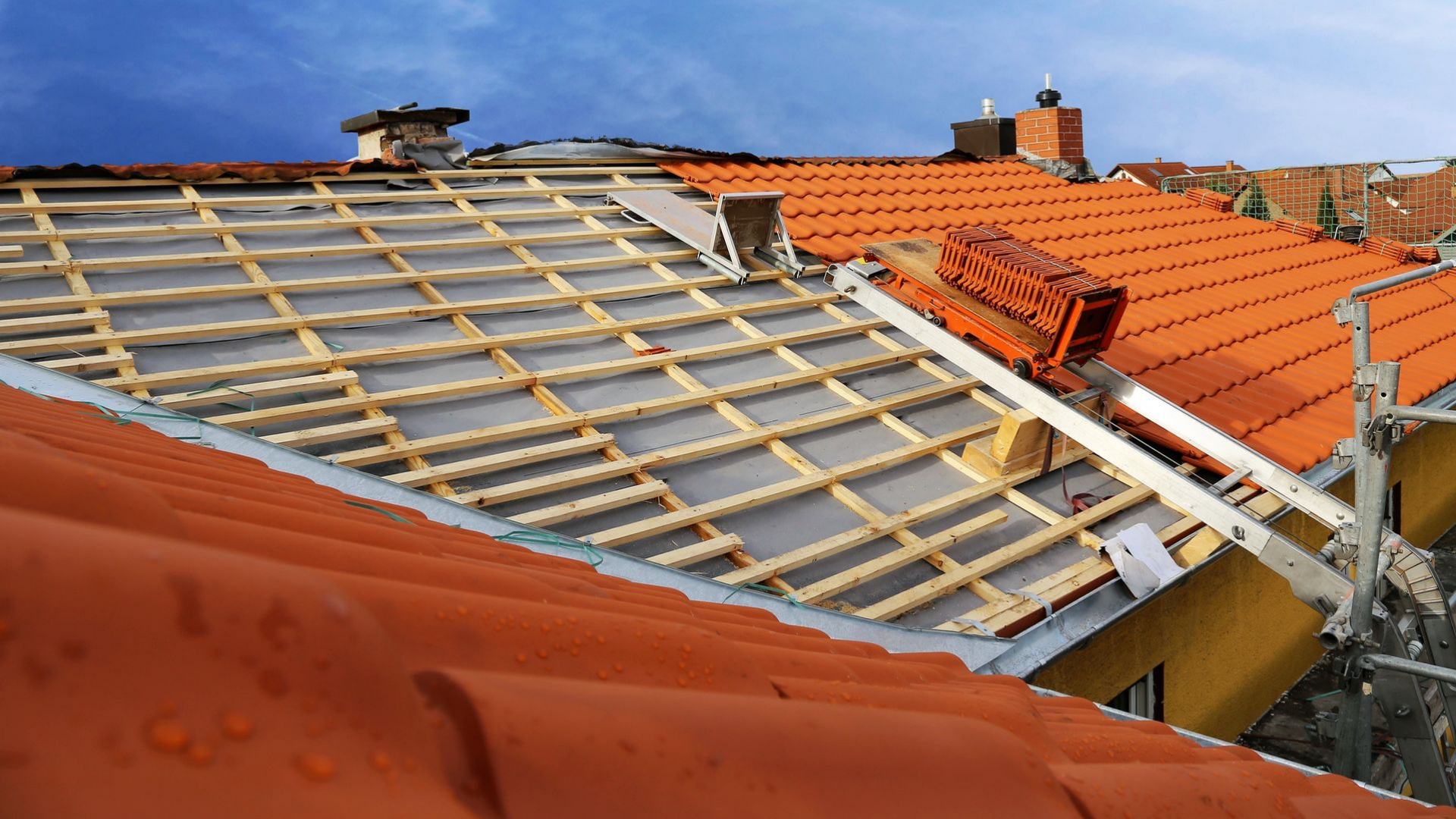 Toit en tuiles orange endommagé, charpente en bois apparente, sous un ciel bleu