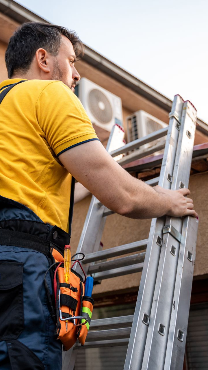 Un couvreur sur une échelle métallique qui inspecte une toiture