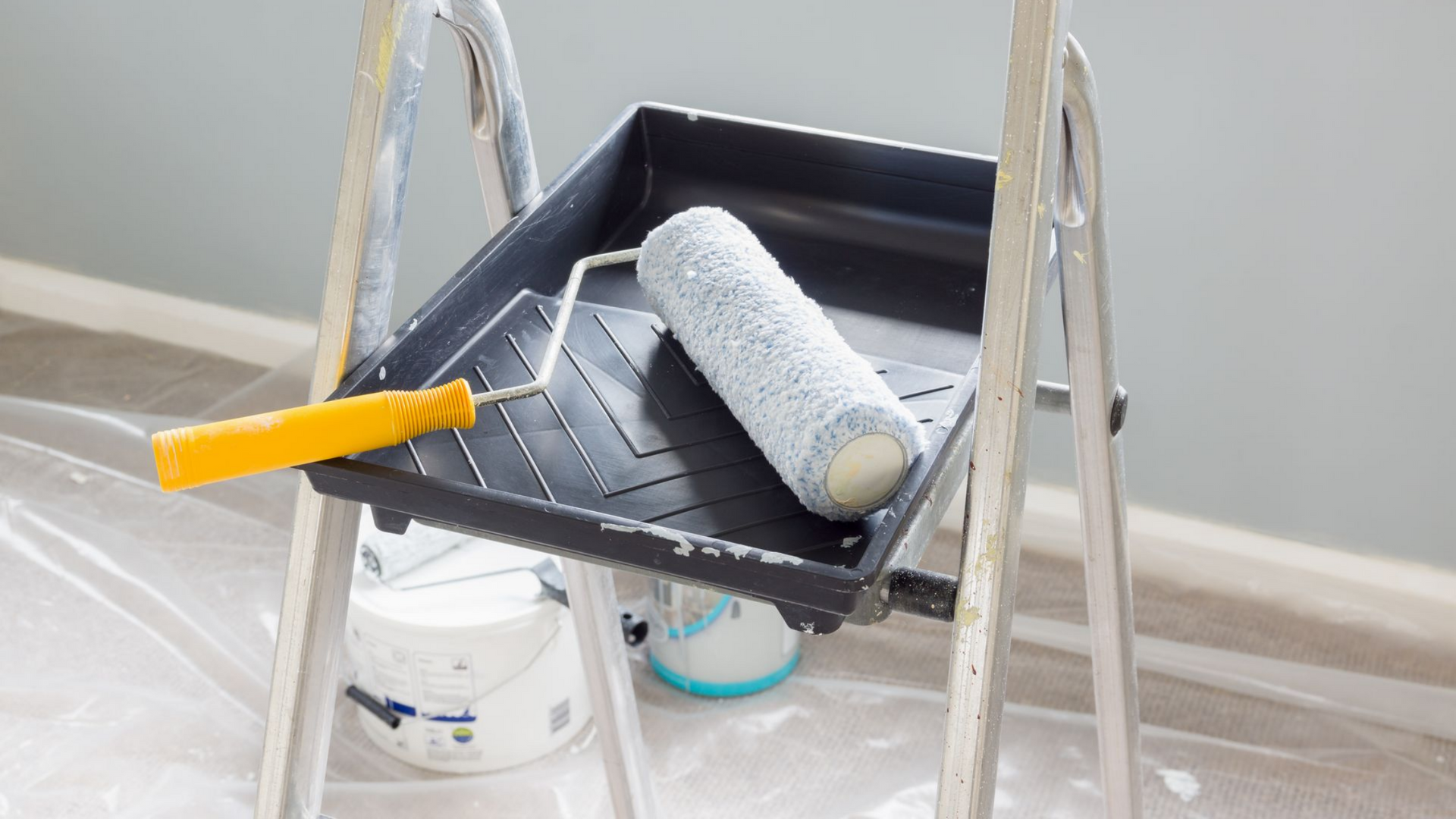 Bac à peinture sur un escabeau avec un rouleau à manche orange dans une pièce en cours de peinture