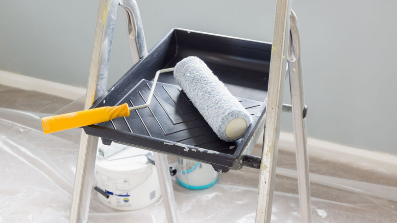 Bac à peinture sur un escabeau avec rouleau et pinceau dans une pièce en rénovation